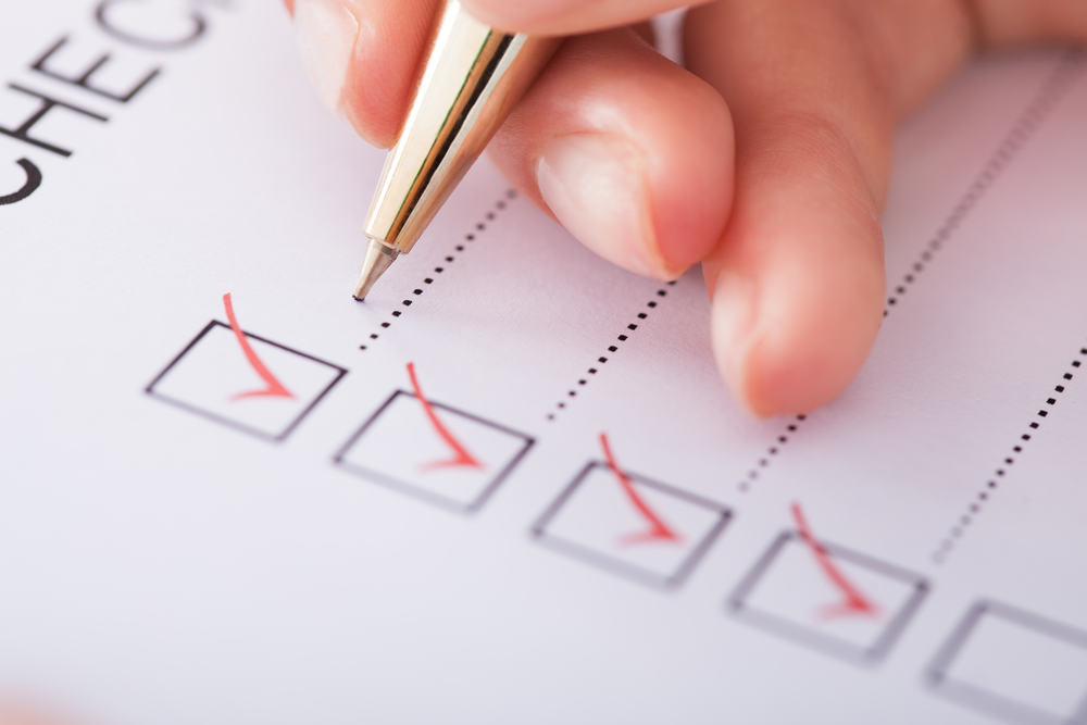checklist paper with red check marks ticked by a hand holding ballpoint pen